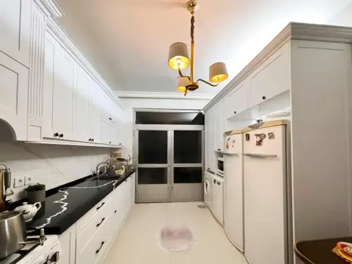 آشپزخانه گالی با کابینت نئوکلاسیک ممبران به رنگ سفید با صفحه کورین مشکی و دستگیره مشکی